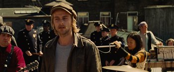 Movie still from “Across the Universe” (2007), directed by Julie Taymor – A man in a leather jacket and a hat is in front of a group of men; Close Up shot, Over the shoulder angle