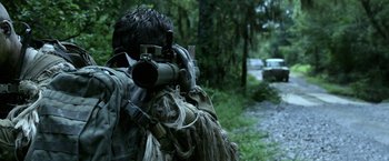 Movie still from “Act of Valor” (2012), directed by Scott Waugh – A man with a rifle in the woods looking at something; Medium shot, Over the shoulder angle