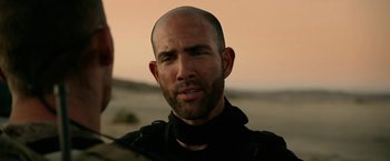 Movie still from “Act of Valor” (2012), directed by Scott Waugh – A man with a bald head is standing in the desert; Close Up shot, Over the shoulder angle
