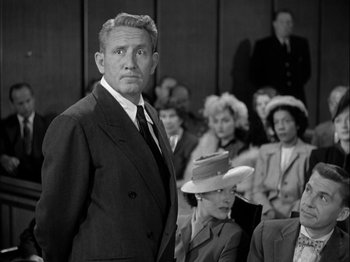 Movie still from “Adam's Rib” (1949), directed by George Cukor – A man in a suit standing in front of a group of people; Medium shot, Over the shoulder angle