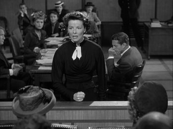 Movie still from “Adam's Rib” (1949), directed by George Cukor – An old photo of a woman standing in front of a group of people; Medium shot, High angle