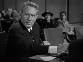 Movie still from “Adam's Rib” (1949), directed by George Cukor – An old photo of a man sitting at a table in front of other people; Medium shot, Over the shoulder angle
