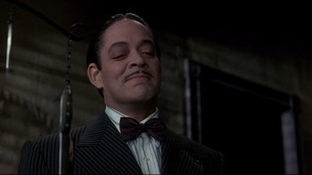 Movie still from “Addams Family Values” (1993), directed by Barry Sonnenfeld – A man in a suit and bow tie smiling for the camera; Close Up shot, Low angle