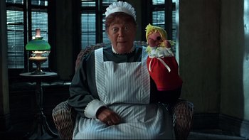 Movie still from “Addams Family Values” (1993), directed by Barry Sonnenfeld – An old woman sitting in a chair holding a doll; Medium shot, High angle