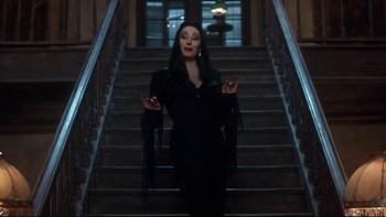 Movie still from “Addams Family Values” (1993), directed by Barry Sonnenfeld – A woman dressed as morticia addams standing on stairs; Medium shot, Low angle