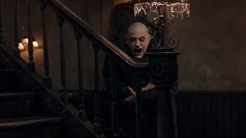 Movie still from “Addams Family Values” (1993), directed by Barry Sonnenfeld – A man with a bald head is standing at the bottom of a staircase; Medium shot, High angle
