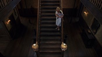 Movie still from “Addams Family Values” (1993), directed by Barry Sonnenfeld – A woman holding a baby on top of a wooden staircase; Wide shot, Overhead angle