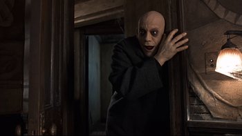 Movie still from “Addams Family Values” (1993), directed by Barry Sonnenfeld – A man with a bald head is standing by a door; Medium shot, Low angle