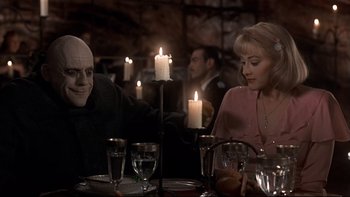 Movie still from “Addams Family Values” (1993), directed by Barry Sonnenfeld – Two people sitting at a dinner table with candles; Medium shot, Over the shoulder angle