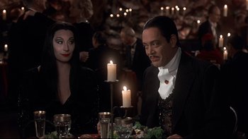 Movie still from “Addams Family Values” (1993), directed by Barry Sonnenfeld – A man and a woman sitting at a dinner table; Medium shot, Over the shoulder angle