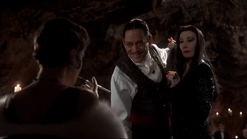 Movie still from “Addams Family Values” (1993), directed by Barry Sonnenfeld – A man and a woman dressed as gomez and morticia addams; Medium shot, Over the shoulder angle