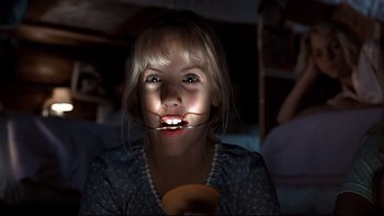 Movie still from “Addams Family Values” (1993), directed by Barry Sonnenfeld – A young girl is holding an orange in her mouth; Close Up shot, Low angle