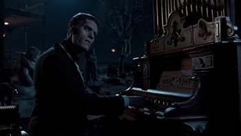 Movie still from “Addams Family Values” (1993), directed by Barry Sonnenfeld – A man sitting in front of an organ in the dark; Medium shot, Low angle
