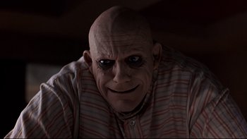 Movie still from “Addams Family Values” (1993), directed by Barry Sonnenfeld – An older bald man with black and red eyes; Close Up shot, Low angle