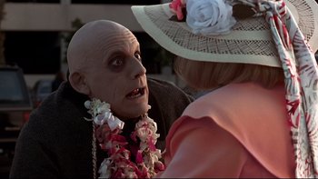 Movie still from “Addams Family Values” (1993), directed by Barry Sonnenfeld – A woman wearing a flower lei talking to an old man; Close Up shot, Over the shoulder angle