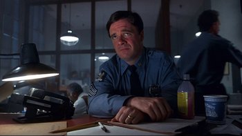 Movie still from “Addams Family Values” (1993), directed by Barry Sonnenfeld – A man sitting at a table in front of papers; Close Up shot, Low angle