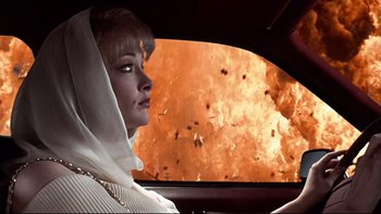 Movie still from “Addams Family Values” (1993), directed by Barry Sonnenfeld – A woman in a car looking out the window at an explosion in the background; Medium shot, Low angle