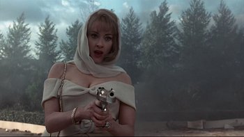 Movie still from “Addams Family Values” (1993), directed by Barry Sonnenfeld – A woman holding a gun while standing in front of trees; Medium shot, Low angle