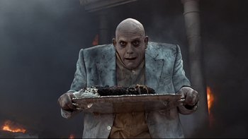 Movie still from “Addams Family Values” (1993), directed by Barry Sonnenfeld – A man holding a tray of food on top of a table; Medium shot, Low angle