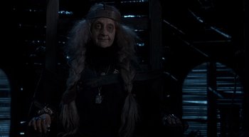 Movie still from “Addams Family Values” (1993), directed by Barry Sonnenfeld – An old woman with long white hair wearing a crown; Medium shot, Over the shoulder angle