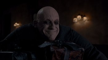 Movie still from “Addams Family Values” (1993), directed by Barry Sonnenfeld – A man with a mask on holding a present; Close Up shot, Over the shoulder angle