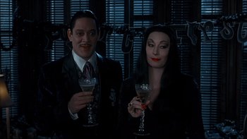 Movie still from “Addams Family Values” (1993), directed by Barry Sonnenfeld – A man and a woman dressed as gomez and morticia addams; Medium shot, High angle