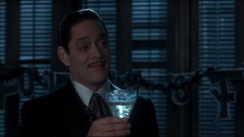 Movie still from “Addams Family Values” (1993), directed by Barry Sonnenfeld – A man in a suit holding a drink in a glass; Close Up shot, Low angle