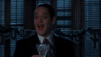Movie still from “Addams Family Values” (1993), directed by Barry Sonnenfeld – A man in a suit and tie holding a glass of wine; Close Up shot, Low angle