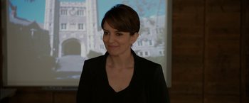 Movie still from “Admission” (2013), directed by Paul Weitz – A woman in a black jacket standing in front of a projection screen; Close Up shot, Over the shoulder angle