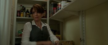 Movie still from “Admission” (2013), directed by Paul Weitz – A woman standing in front of shelves in a kitchen; Medium shot, Over the shoulder angle