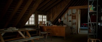 Movie still from “Admission” (2013), directed by Paul Weitz – A man sitting at a wooden desk in a room; Wide shot, High angle