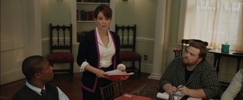Movie still from “Admission” (2013), directed by Paul Weitz – A woman standing in front of a table holding a book; Medium shot, Over the shoulder angle
