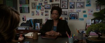 Movie still from “Admission” (2013), directed by Paul Weitz – A woman sitting at a table in front of pictures; Medium shot, Over the shoulder angle