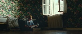 Movie still from “Adoration” (2019), directed by Fabrice du Welz – A boy sitting on a couch reading a book; Wide shot, High angle