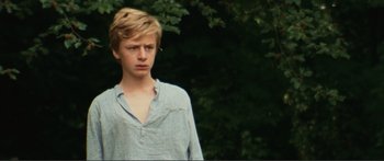 Movie still from “Adoration” (2019), directed by Fabrice du Welz – A young man standing in front of a tree; Medium shot, Low angle