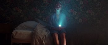 Movie still from “Adoration” (2019), directed by Fabrice du Welz – A woman sitting on a bed holding a flashlight; Medium shot, Overhead angle