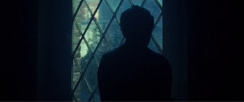 Movie still from “Adoration” (2019), directed by Fabrice du Welz – A man looking out a window at a fish tank; Medium shot, Over the shoulder angle