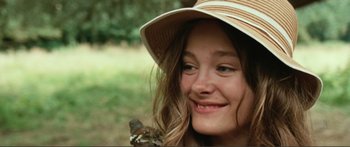 Movie still from “Adoration” (2019), directed by Fabrice du Welz – A young girl wearing a sun hat with a cat on her shoulder; Close Up shot, Over the shoulder angle
