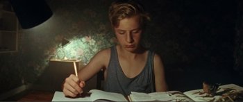 Movie still from “Adoration” (2019), directed by Fabrice du Welz – A boy is reading a book in a dark room; Close Up shot, High angle