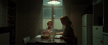 Movie still from “Adoration” (2019), directed by Fabrice du Welz – A man and a woman sitting at a table with a cake; Medium shot, High angle
