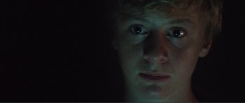 Movie still from “Adoration” (2019), directed by Fabrice du Welz – A young man stares into the camera in the dark; Extreme Close Up shot, Low angle
