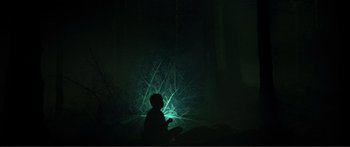 Movie still from “Adoration” (2019), directed by Fabrice du Welz – A person sitting in a dark room with a light on; Extreme Wide shot, Low angle