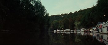 Movie still from “Adoration” (2019), directed by Fabrice du Welz – A body of water surrounded by trees and a forest; Extreme Wide shot, High angle