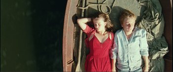 Movie still from “Adoration” (2019), directed by Fabrice du Welz – A woman in a red dress leaning against a wall with a boy; Medium shot, Overhead angle