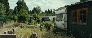 Movie still from “Adoration” (2019), directed by Fabrice du Welz – An old trailer is parked in the middle of a field; Extreme Wide shot, High angle