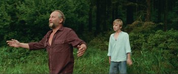 Movie still from “Adoration” (2019), directed by Fabrice du Welz – Two people standing in the grass near a forest; Medium shot, Low angle