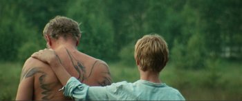 Movie still from “Adoration” (2019), directed by Fabrice du Welz – Two men sitting on a bench looking out at the woods; Medium shot, Over the shoulder angle