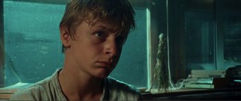 Movie still from “Adoration” (2019), directed by Fabrice du Welz – A young man looking at the camera in front of a window; Close Up shot, Low angle