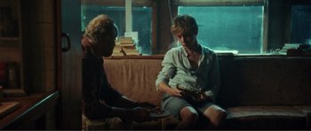 Movie still from “Adoration” (2019), directed by Fabrice du Welz – Two people sitting on a couch in front of a window; Medium shot, Over the shoulder angle