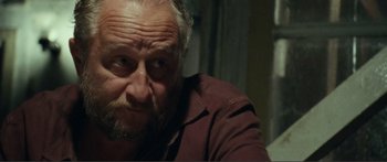 Movie still from “Adoration” (2019), directed by Fabrice du Welz – An old man with a beard and a brown shirt; Close Up shot, Over the shoulder angle